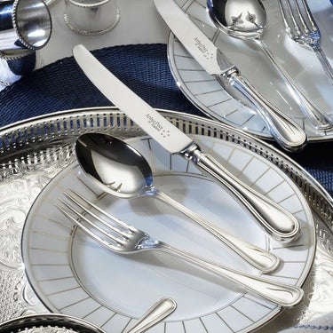 Silver cutlery set on decorative plates with a blue napkin underneath.