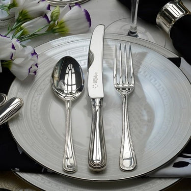 Silver cutlery set on a decorative plate with flowers in the background