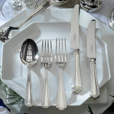 Silver cutlery set on a white plate with a decorative background