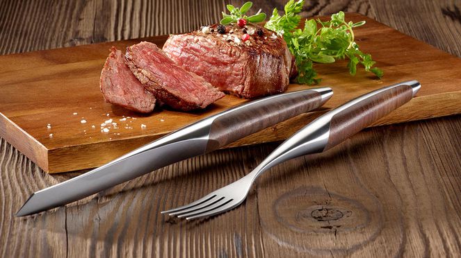 Steak with walnut knife and fork on wooden board